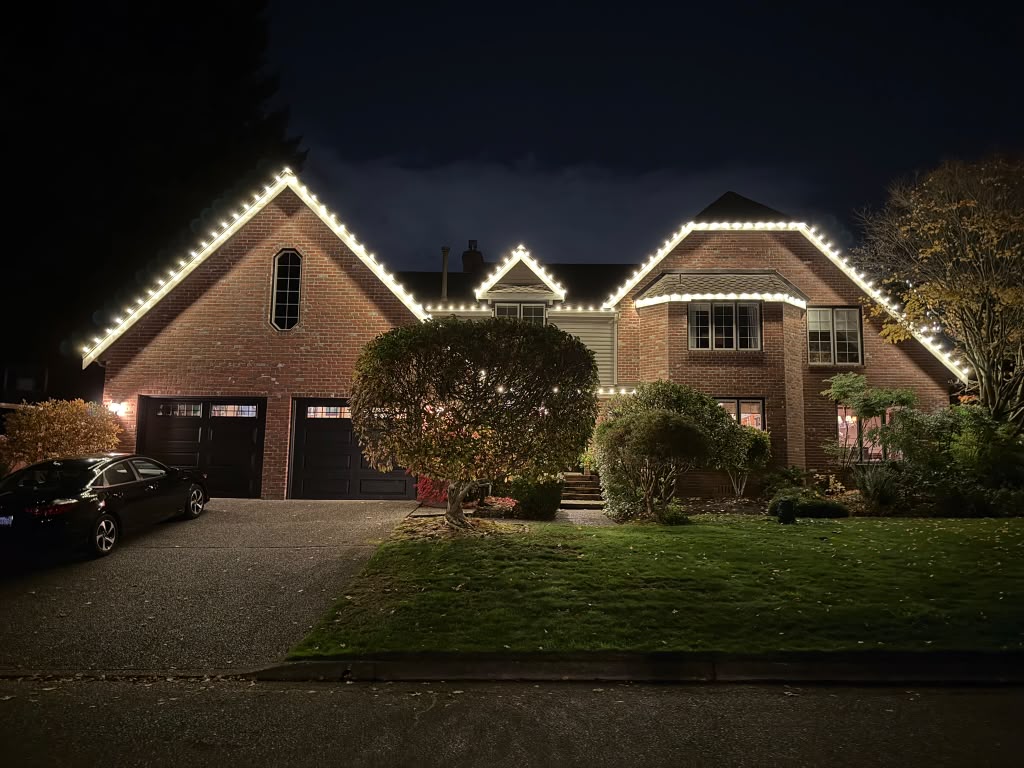 Brick home with a clean line of white lights along the roofline at night