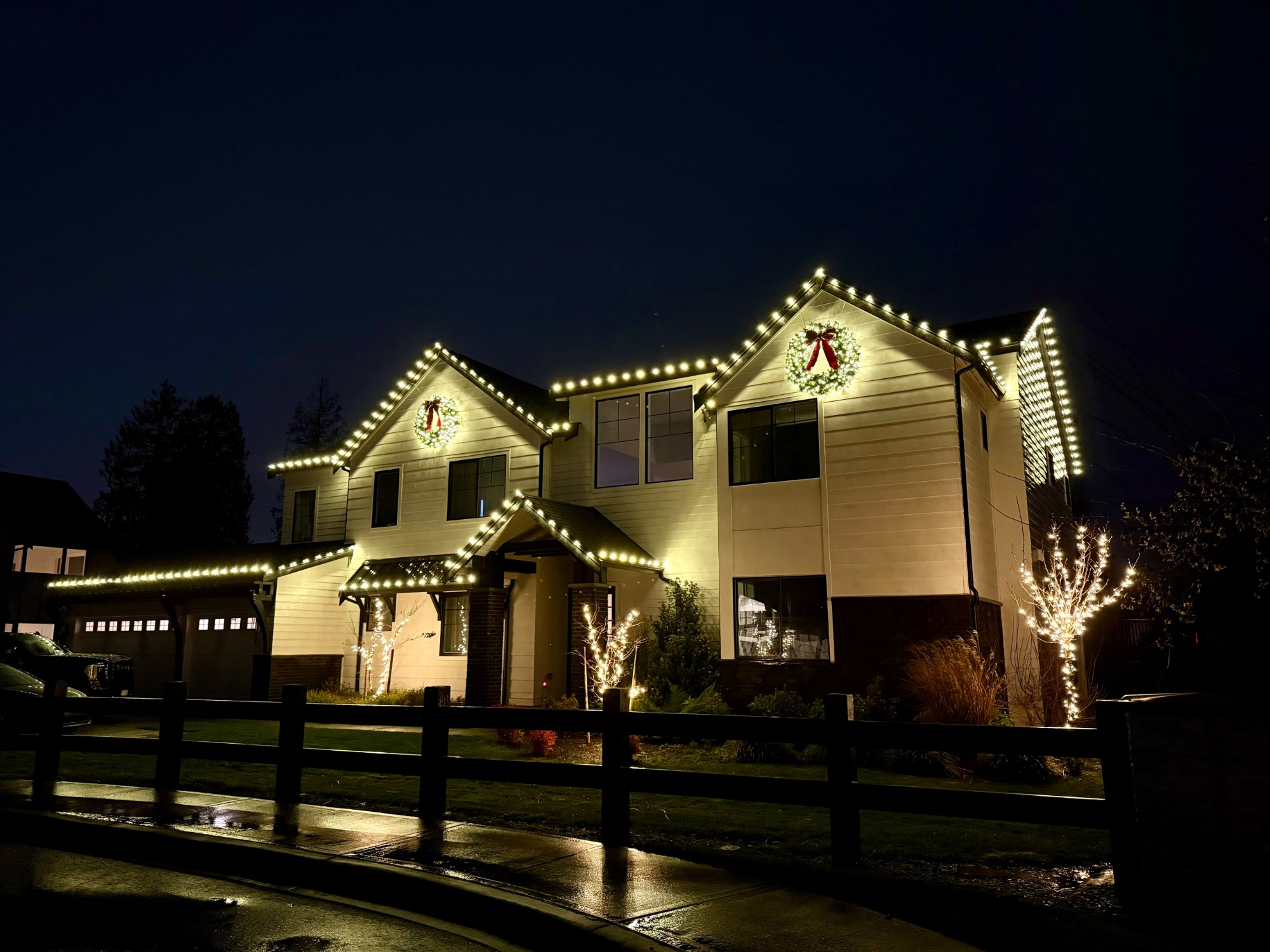 Two-story home with roofline lights, wreaths and lit trees at night