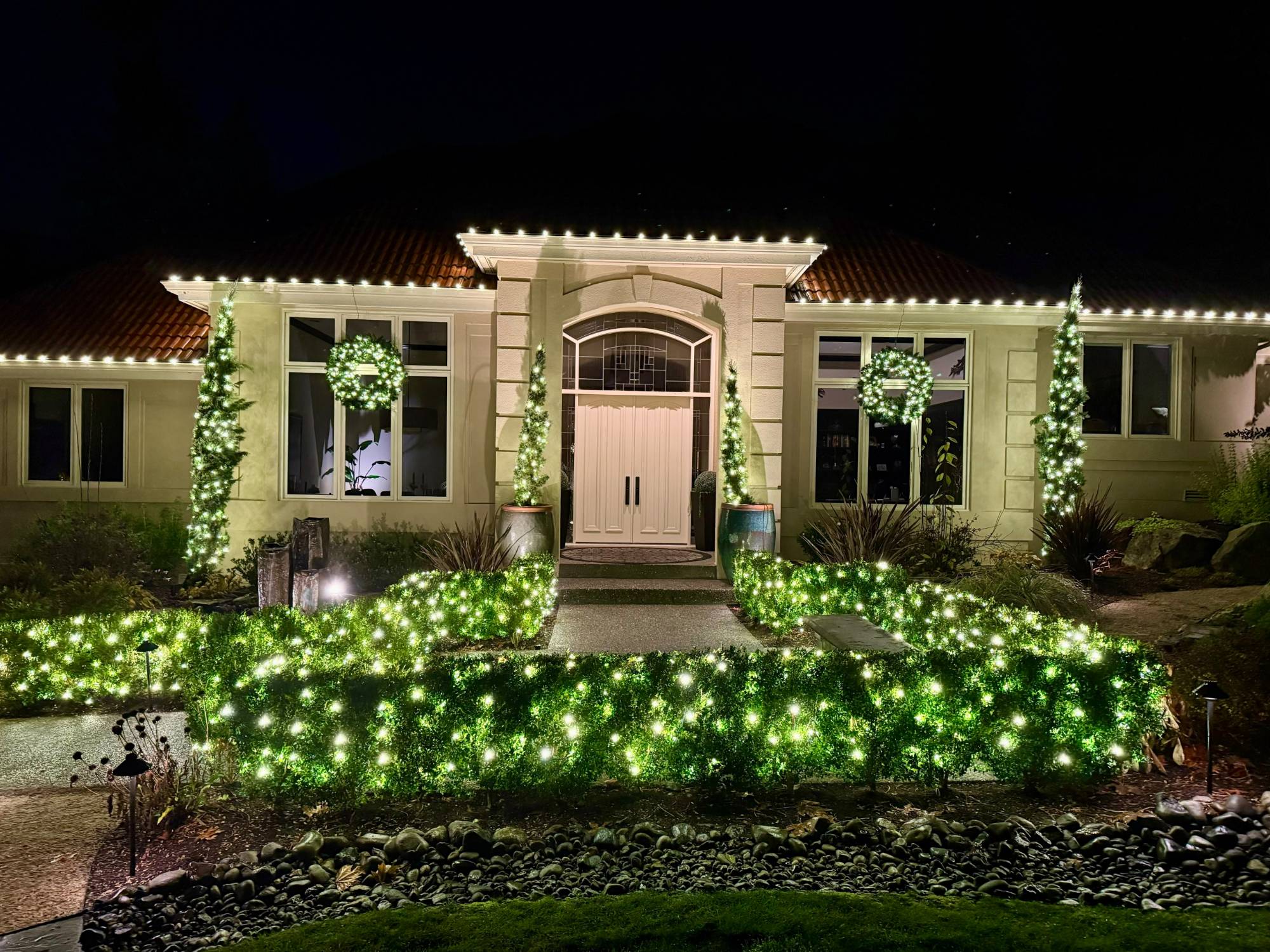 Home entrance with roofline lights, lit wreaths, topiaries and hedges at night