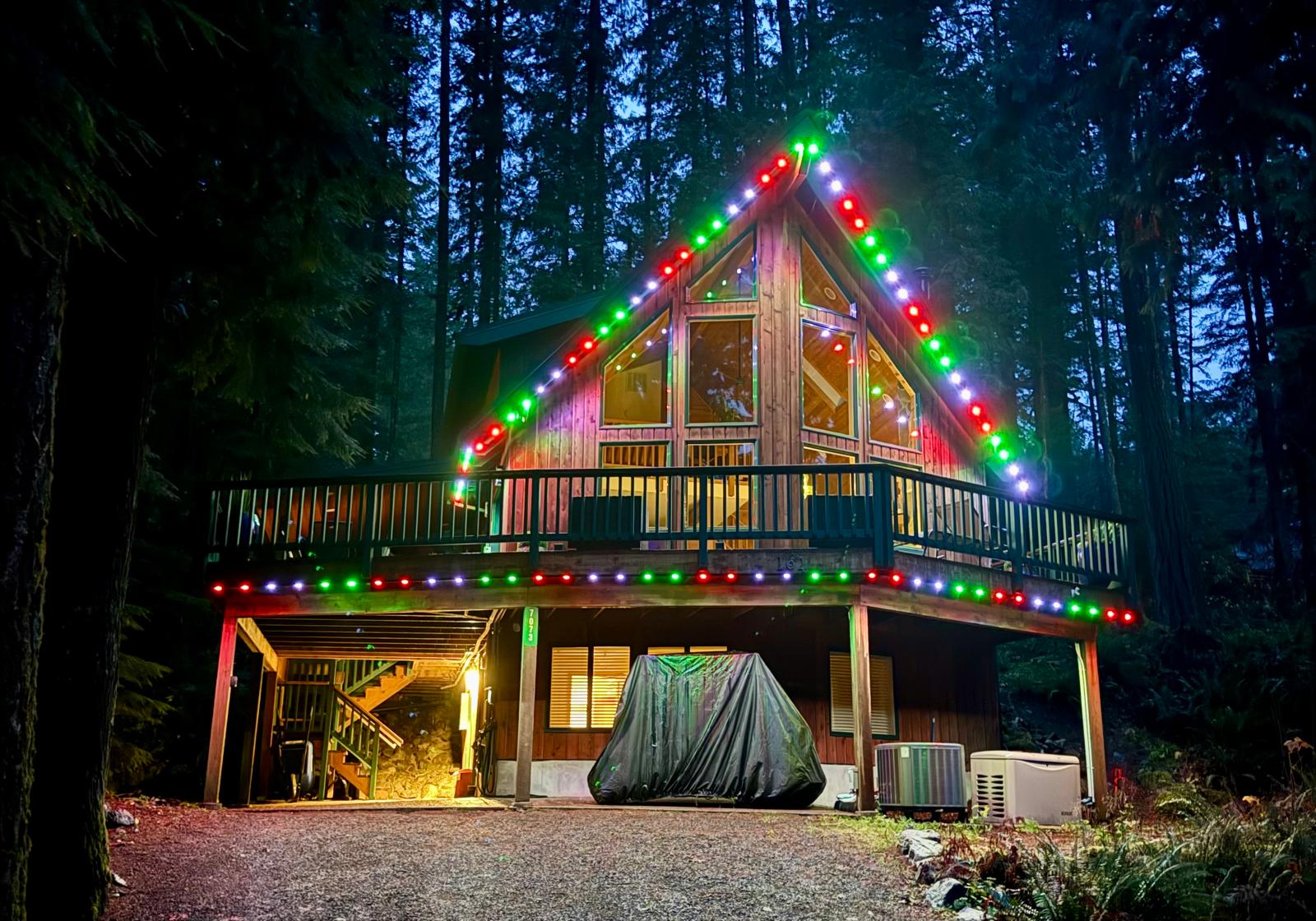 Forest cabin with green, red and white permanent lights along the roof and deck