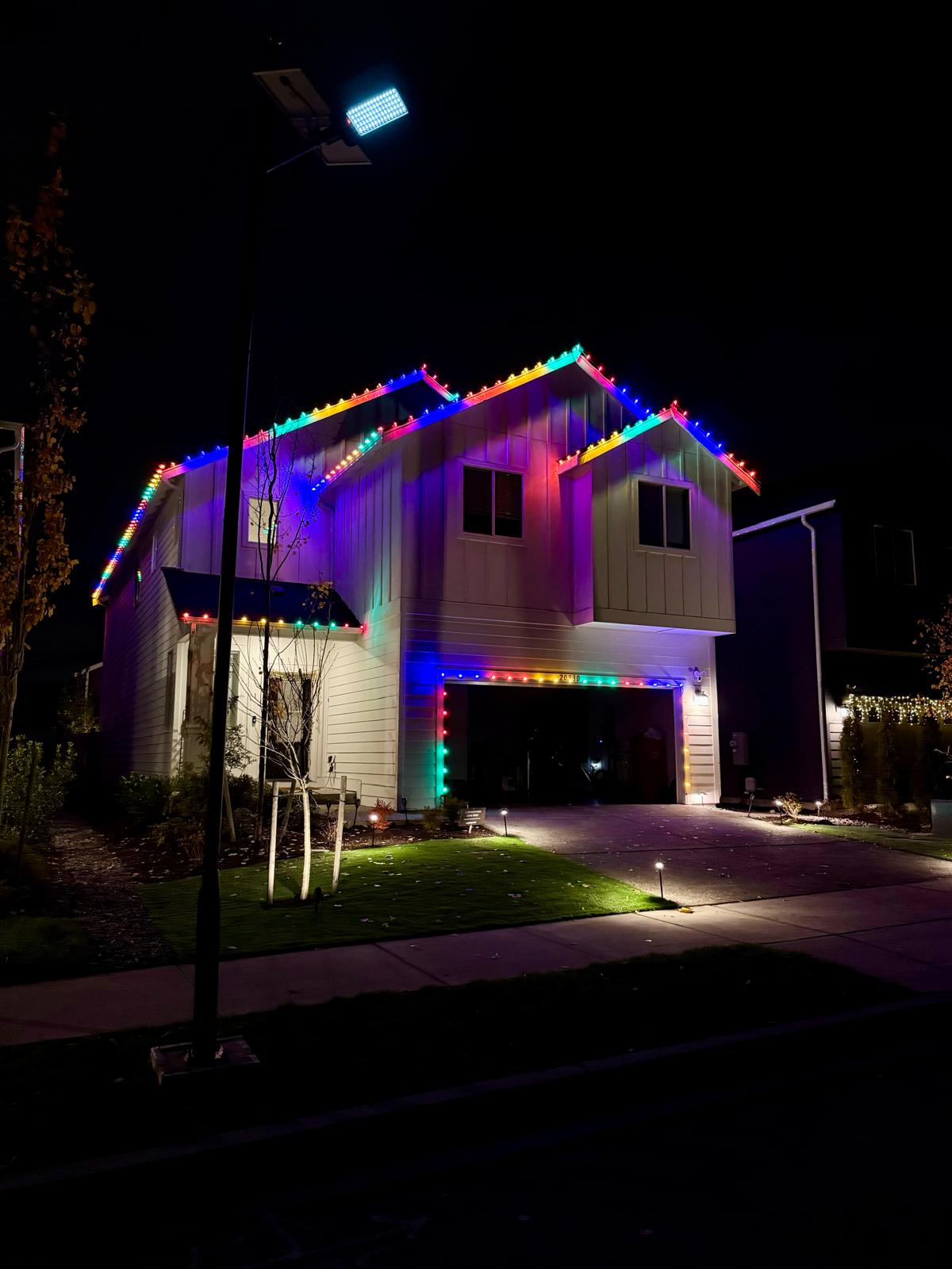 Two-story home with multicolor permanent lights along the roofline and garage at night