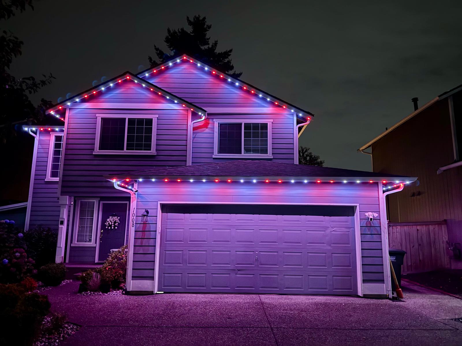 Two-story home with red and white permanent lights along the roofline and garage